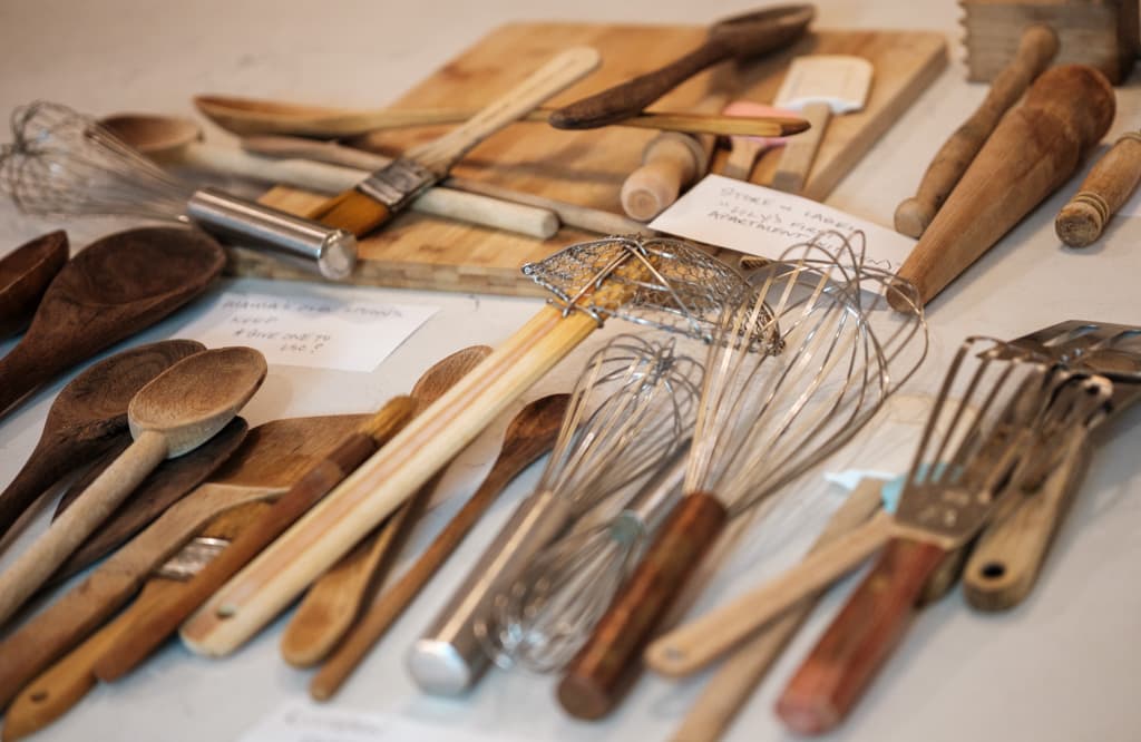 Wooden spoons, whisks and rolling pins sorted across a table, with handwritten notes marking what to keep and what to pass on.